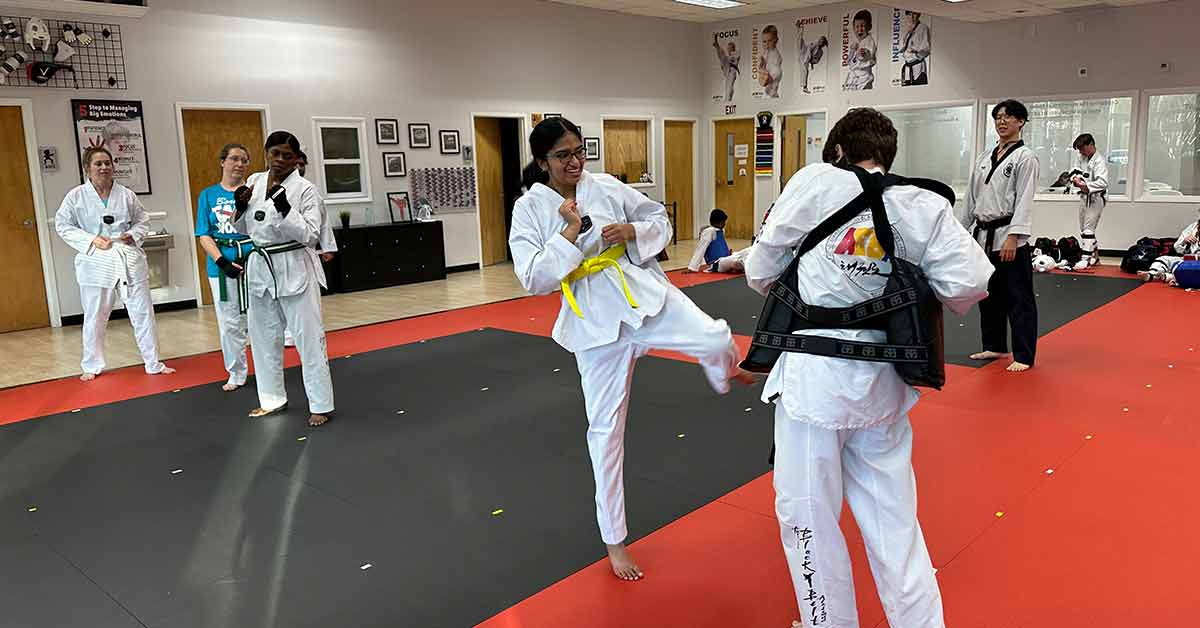 a student is kicking a target which a black belt is holding