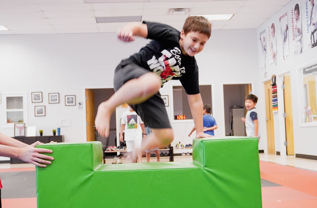 Smiling child jumping over a ninja obstacle during summer camp at ABBA Martial Arts in Peachtree City.