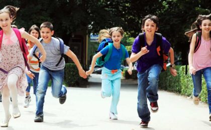 Group of smiling kids with backpacks running outdoors on their first day back to school in Peachtree City