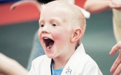 Young child smiling excitedly during a kids martial arts class for ages 4–6.