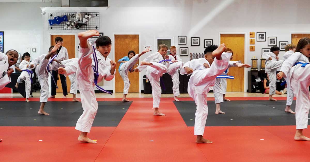 Kids practicing high kicks in a Taekwondo class, building focus and balance