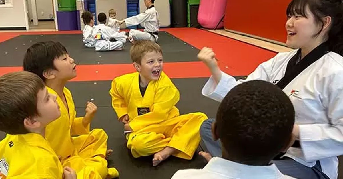 Young children in Taekwondo class sitting with an instructor, building confidence and overcoming separation anxiety