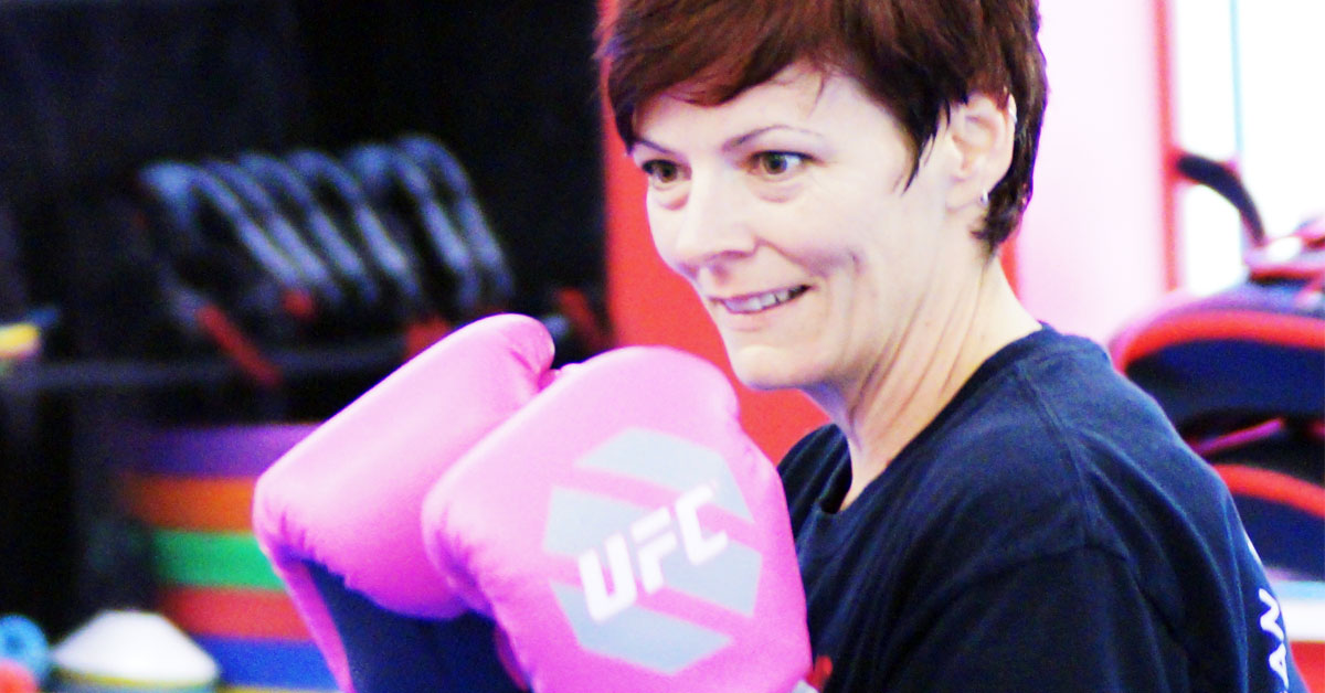 Taekwondo training for moms in Peachtree City Smiling mom in boxing gloves posing in guard stance during taekwondo class in Peachtree City