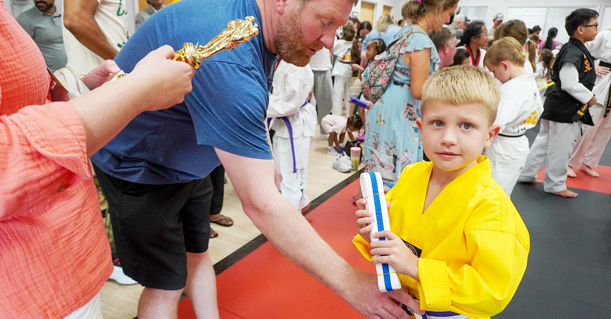 A proud child earning their Taekwondo belt, symbolizing lifelong confidence and discipline.