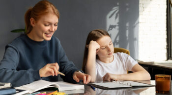 Tired student getting homework help from a smiling teacher at the table